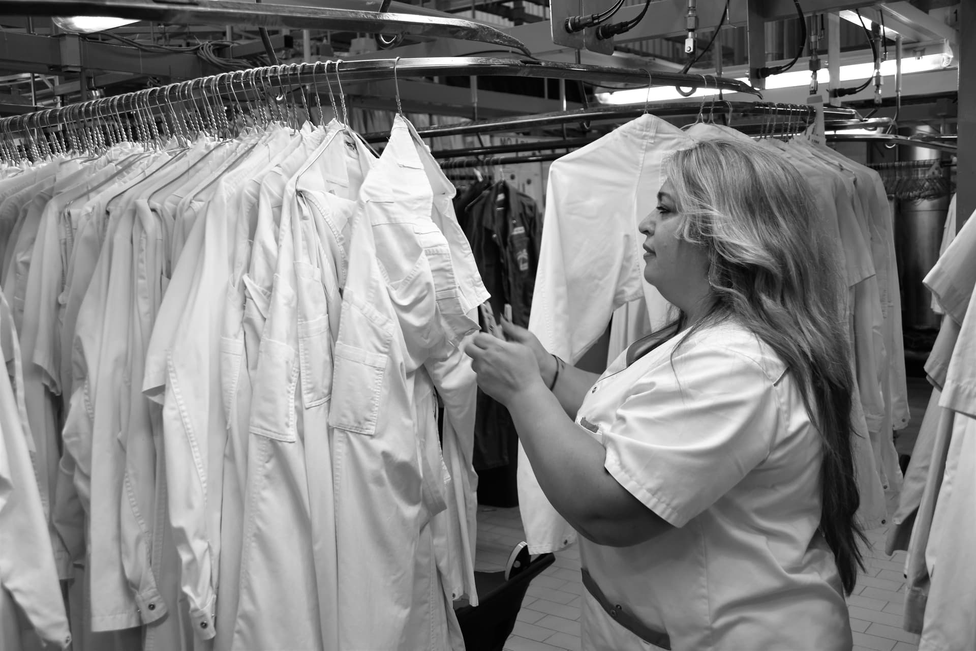 Professional worker in white uniform carefully inspecting blue dress shirt under bright lighting